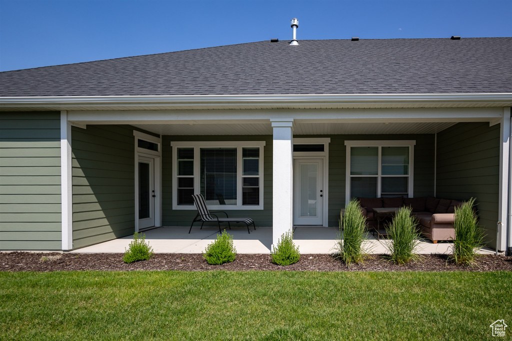 Doorway to property with a shingled roof, covered porch, a yard, and outdoor lounge area