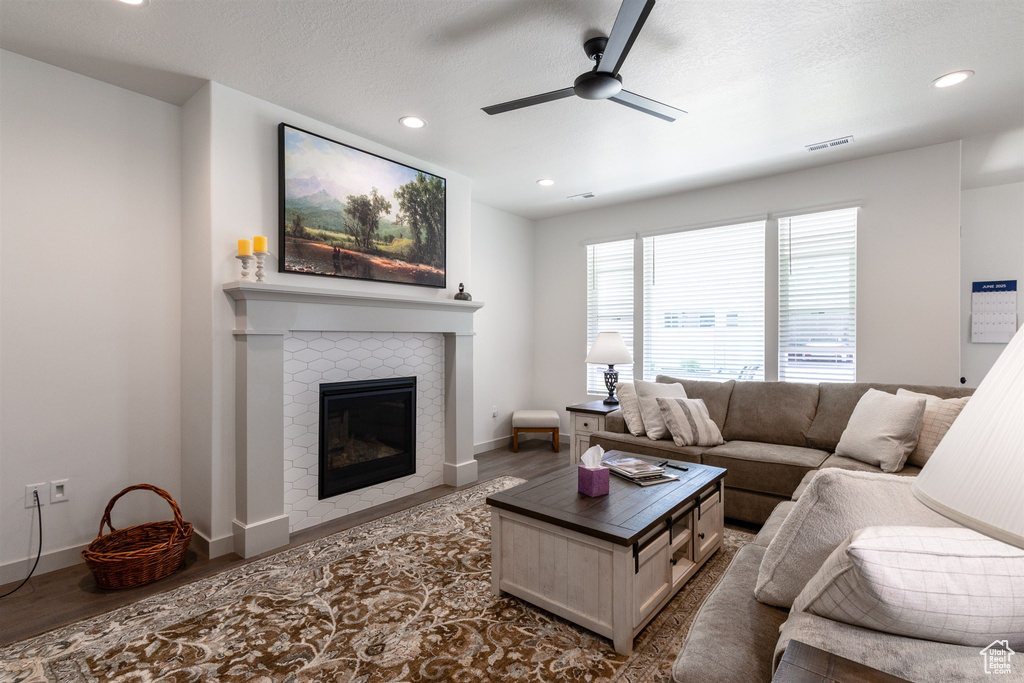 Living room with a ceiling fan, a tiled fireplace, recessed lighting, wood finished floors, and baseboards