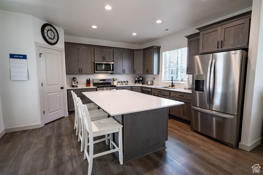 Kitchen featuring appliances with stainless steel finishes, dark brown cabinets, decorative backsplash, a sink, and baseboards