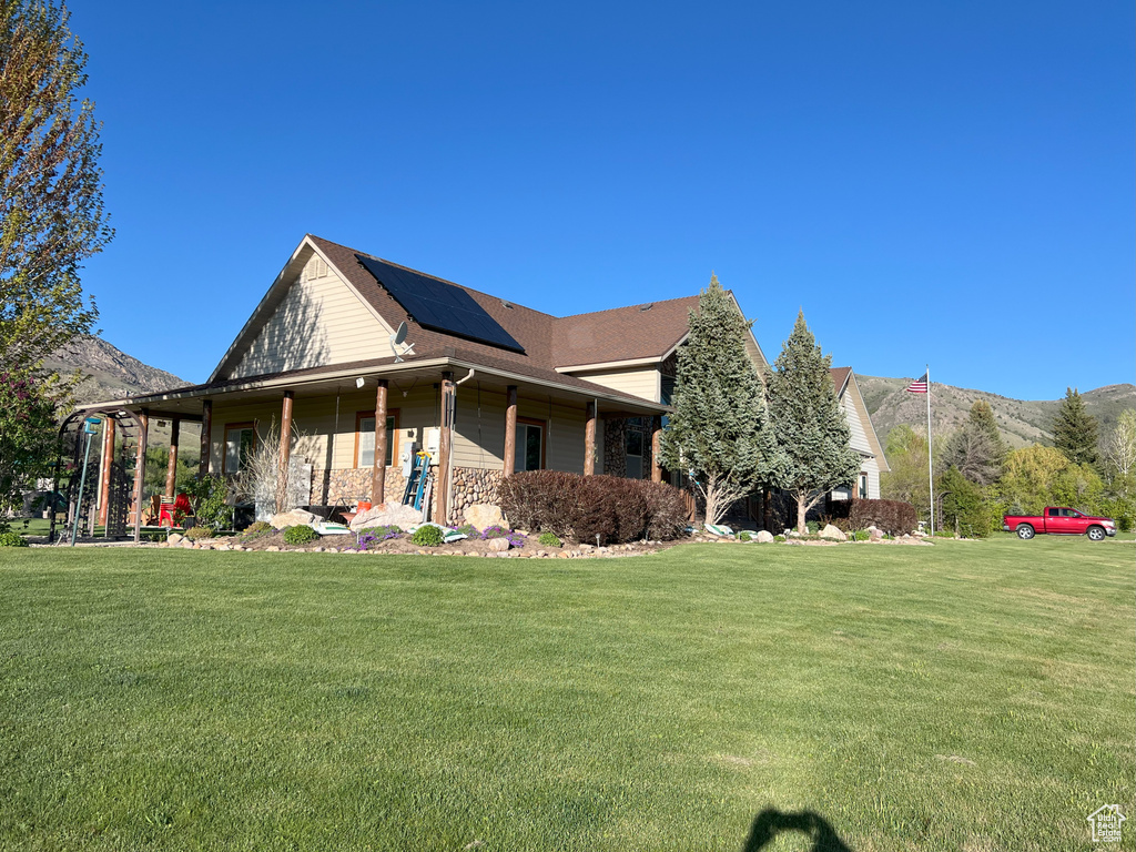 Farmhouse-style home with roof mounted solar panels, a front lawn, a mountain view, and covered porch