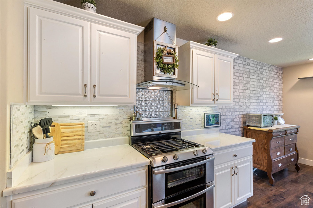Kitchen featuring range with two ovens, white cabinetry, wall chimney range hood, tasteful backsplash, and recessed lighting