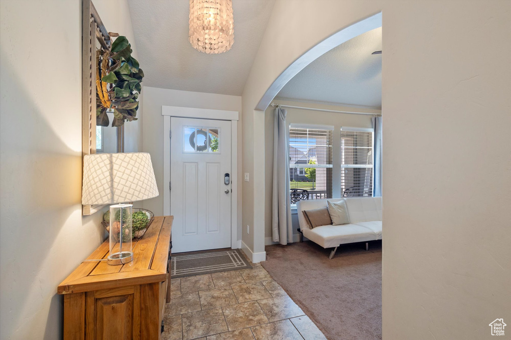 Carpeted foyer with arched walkways, baseboards, a chandelier, and stone finish floors