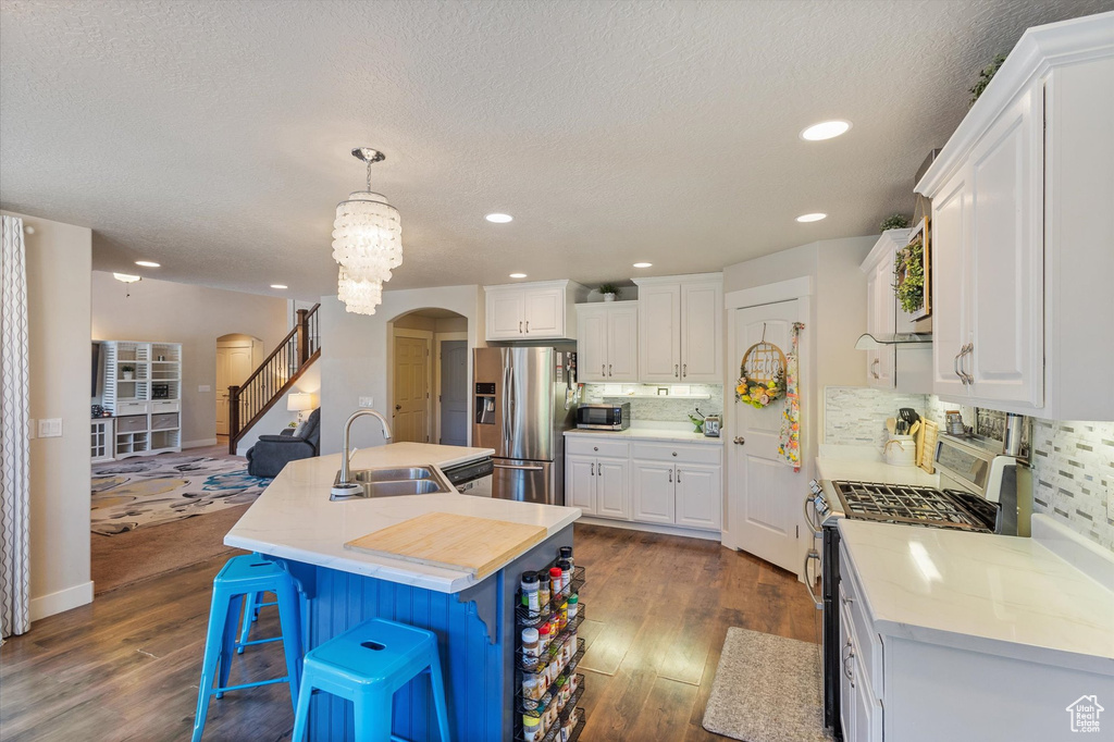 Kitchen with stainless steel appliances, a sink, arched walkways, dark wood finished floors, and a textured ceiling