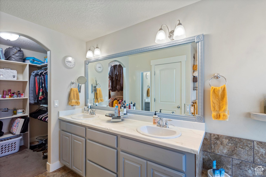 Bathroom with double vanity, a textured ceiling, and a walk in closet