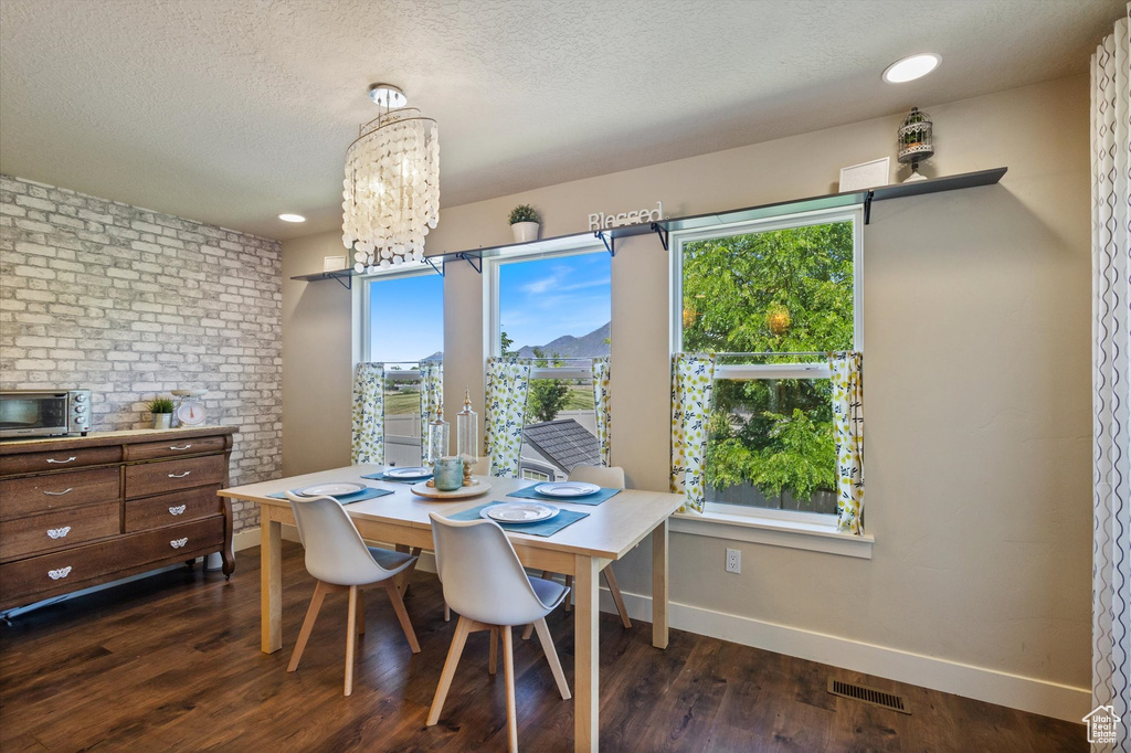 Dining area featuring baseboards, dark wood-type flooring, a chandelier, and a textured ceiling