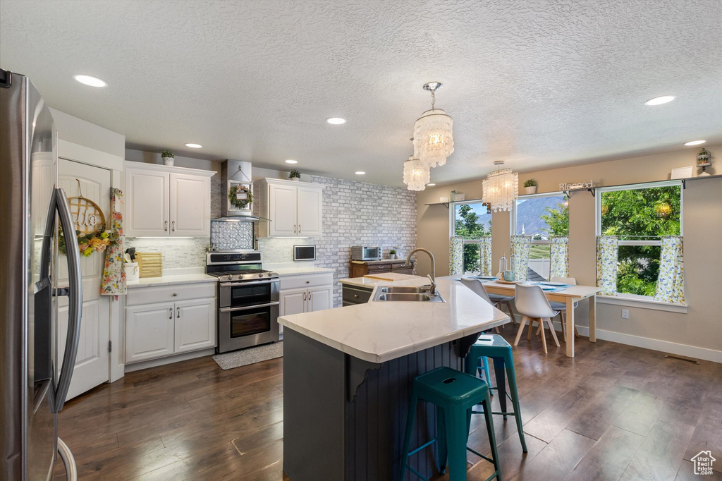 Kitchen featuring stainless steel appliances, wall chimney range hood, a sink, a chandelier, and light countertops