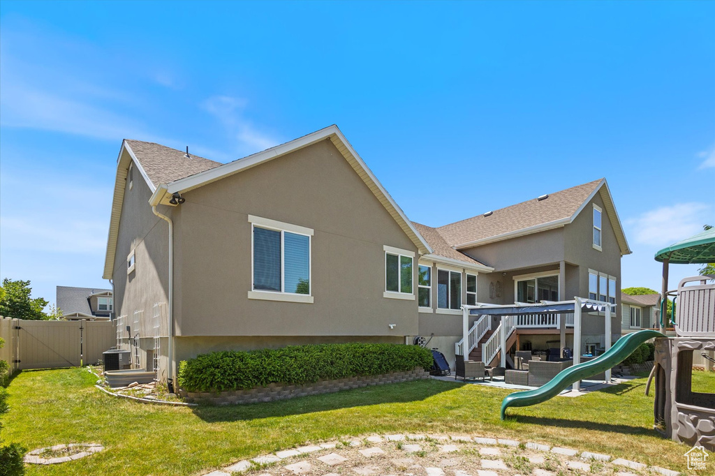 Rear view of house featuring stucco siding, a playground, a gate, central air condition unit, and a shingled roof