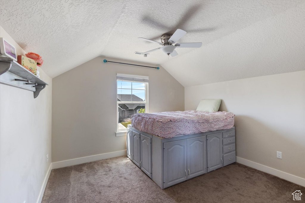 Bedroom with vaulted ceiling, a textured ceiling, light colored carpet, ceiling fan, and baseboards