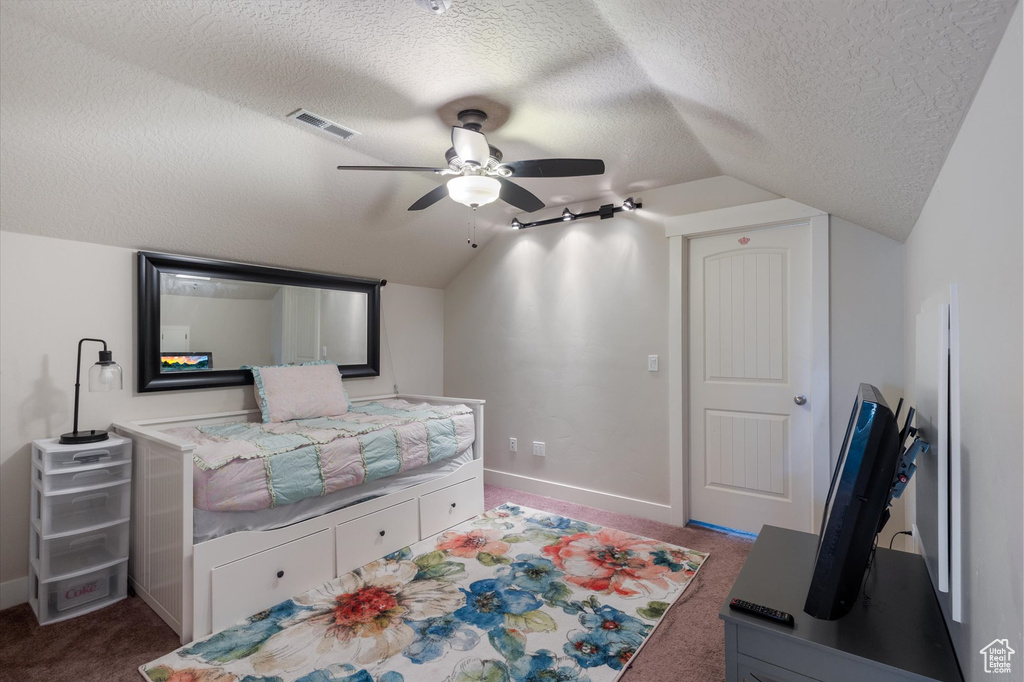 Carpeted bedroom featuring vaulted ceiling, a textured ceiling, baseboards, and a ceiling fan