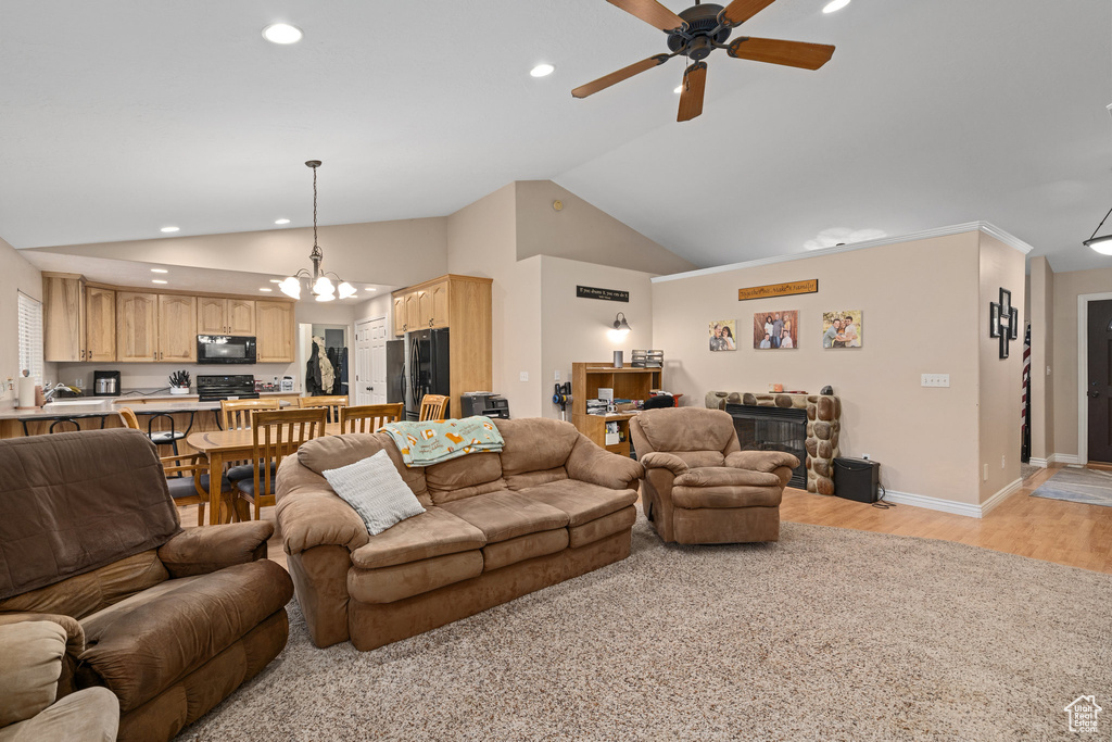 Living room with lofted ceiling, ceiling fan, recessed lighting, light wood finished floors, and a chandelier