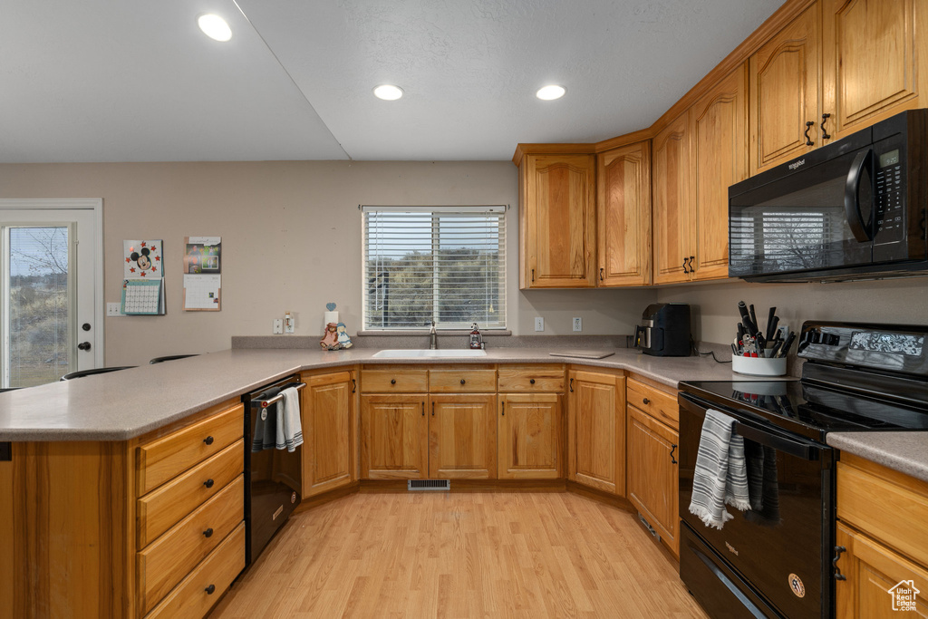 Kitchen featuring black appliances, a sink, a peninsula, light wood-type flooring, and light countertops