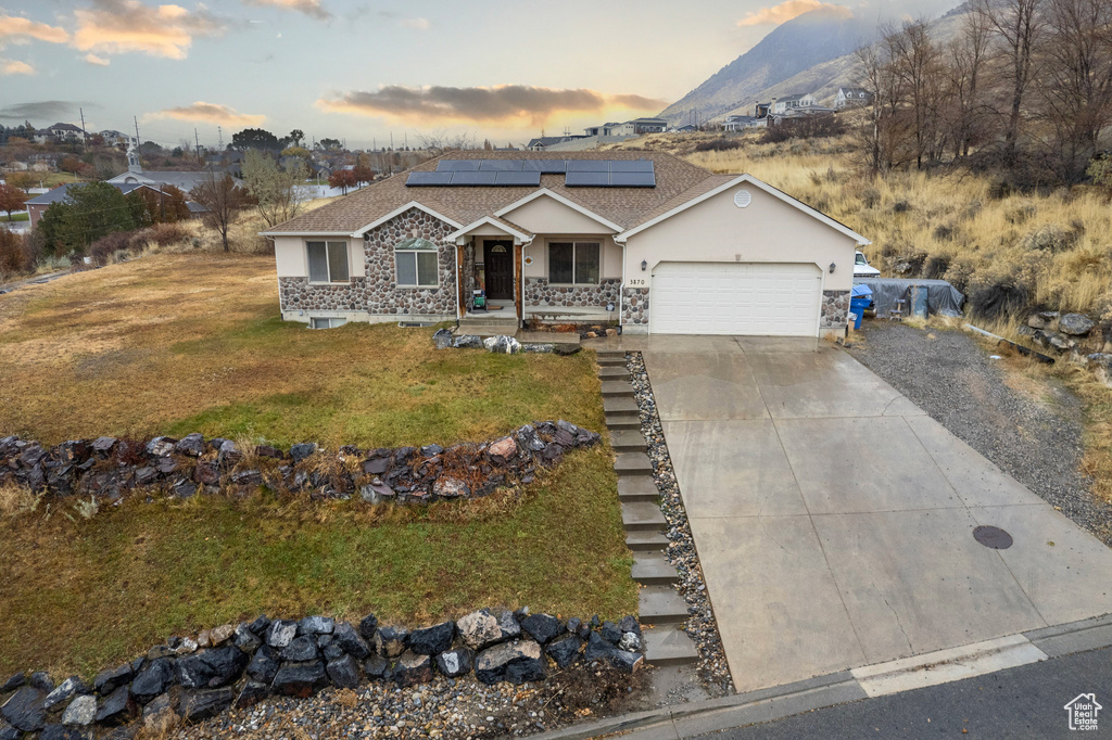 Single story home featuring an attached garage, concrete driveway, a lawn, roof mounted solar panels, and stucco siding