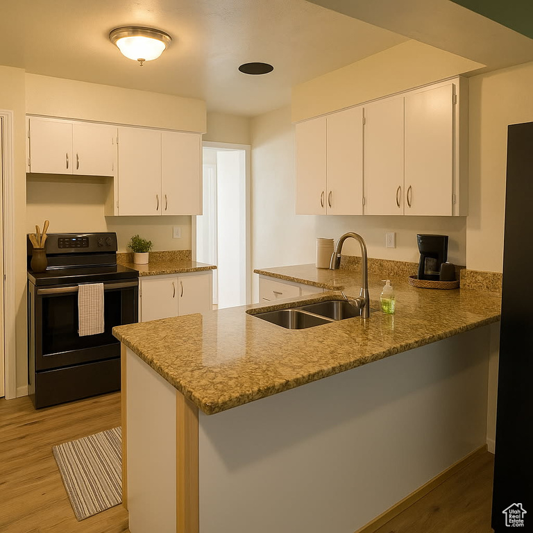 Kitchen with electric range, a sink, light stone counters, light wood-style floors, and white cabinets