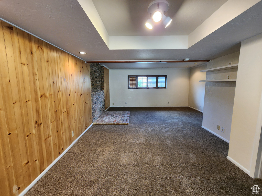 Unfurnished bedroom featuring dark colored carpet, wood walls, baseboards, and a raised ceiling