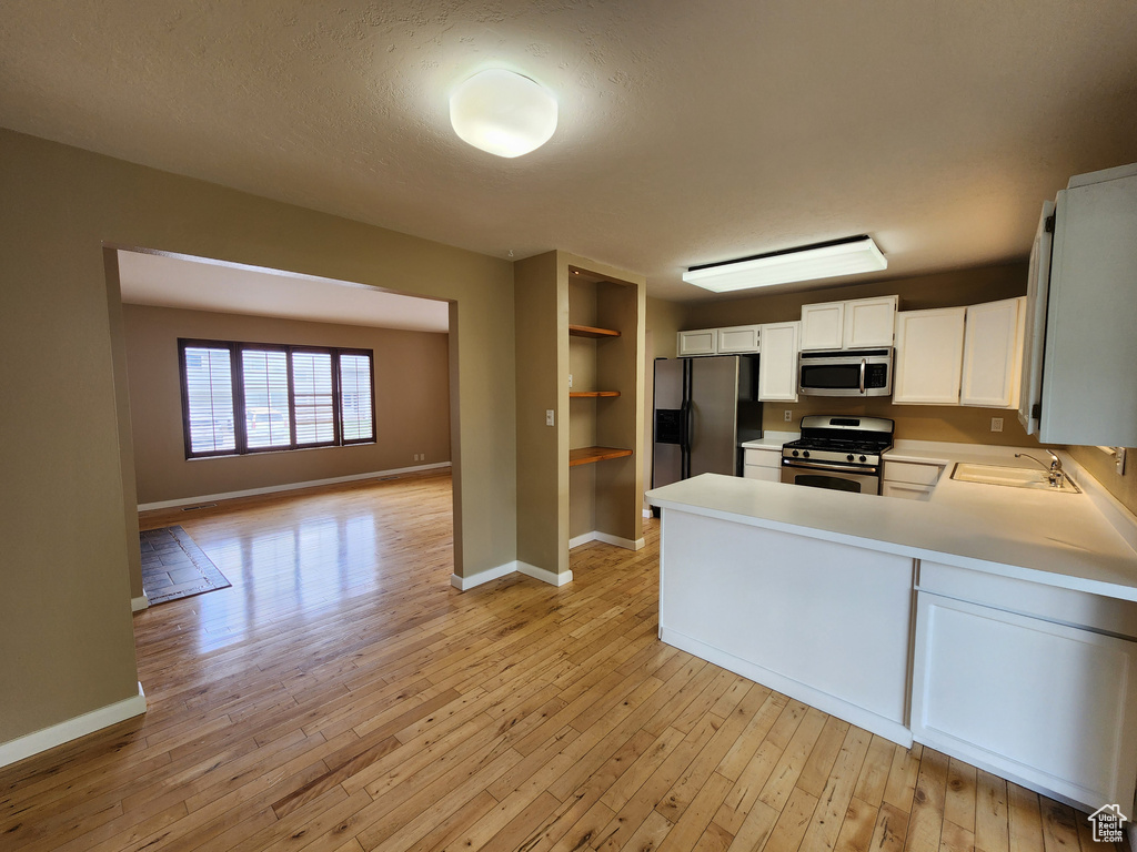Kitchen featuring stainless steel appliances, light wood finished floors, light countertops, a peninsula, and baseboards