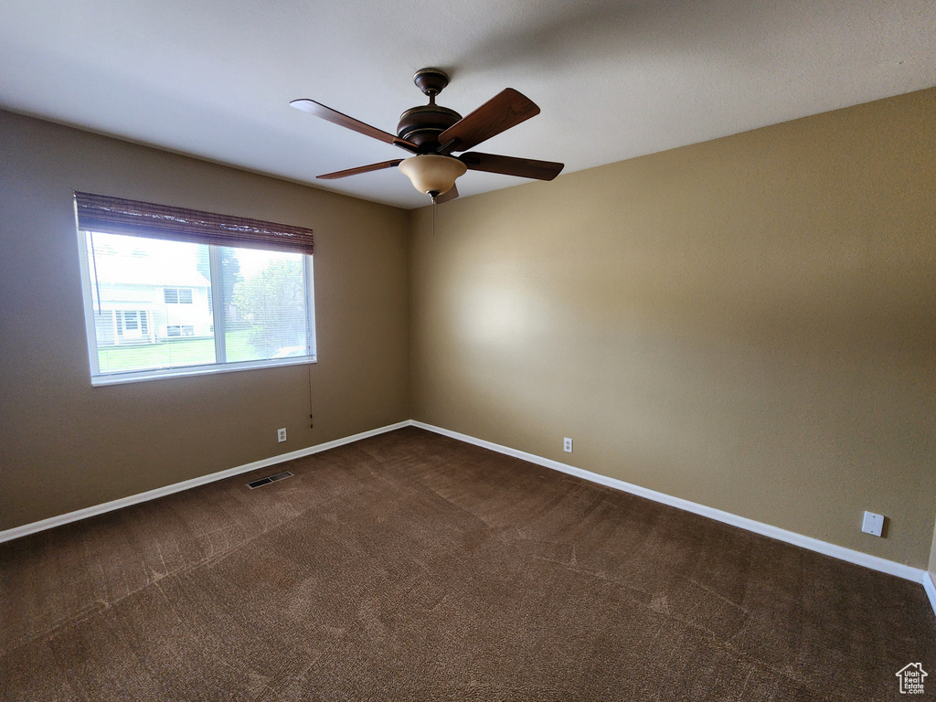 Unfurnished room featuring ceiling fan, dark colored carpet, and baseboards