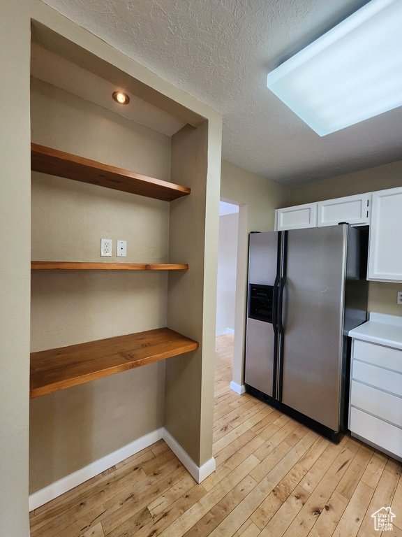 Kitchen with stainless steel fridge, light wood-style floors, white cabinetry, baseboards, and a textured ceiling