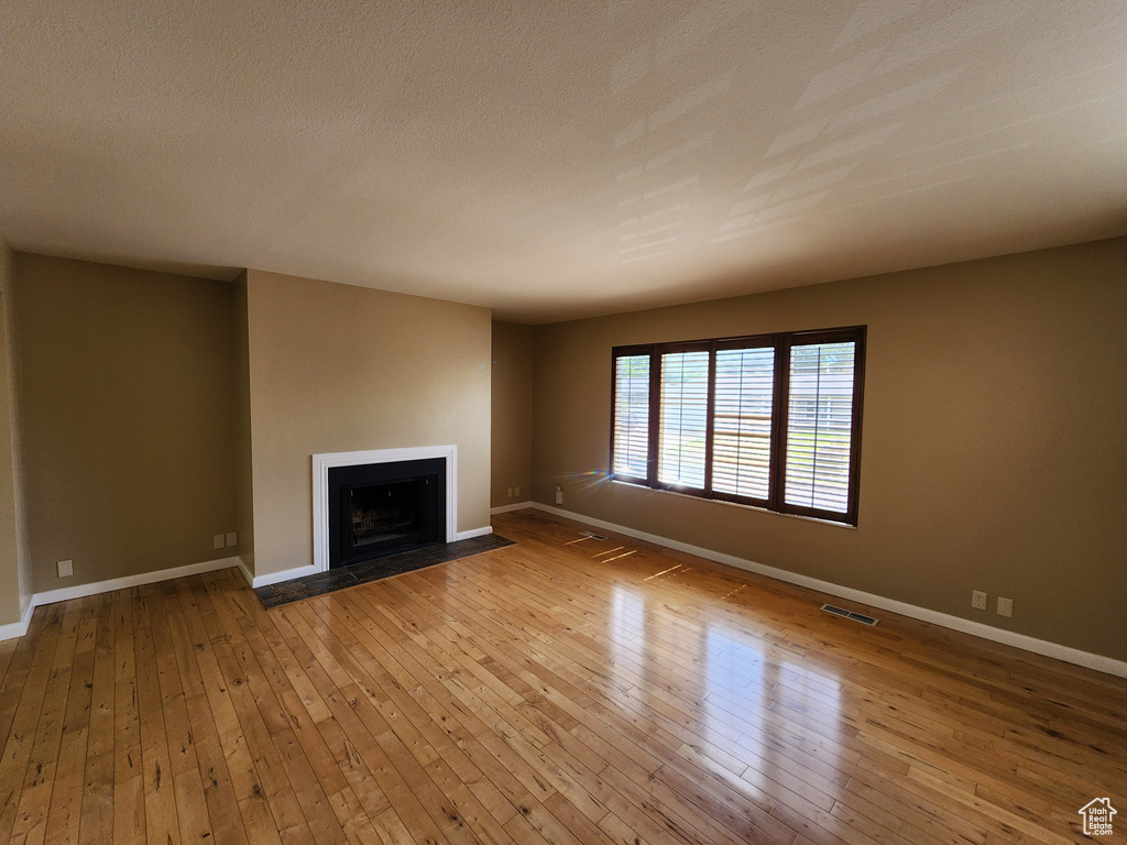 Unfurnished living room featuring a fireplace with flush hearth, baseboards, and hardwood / wood-style floors