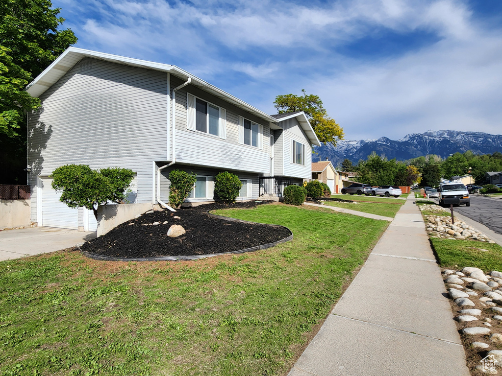 View of side of home with a yard, a mountain view, driveway, and an attached garage