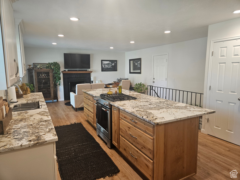 Kitchen with stainless steel gas range oven, light wood-type flooring, a sink, recessed lighting, and a fireplace