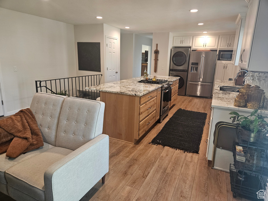 Kitchen featuring stainless steel appliances, a sink, stacked washing machine and dryer, light wood-style floors, and a center island