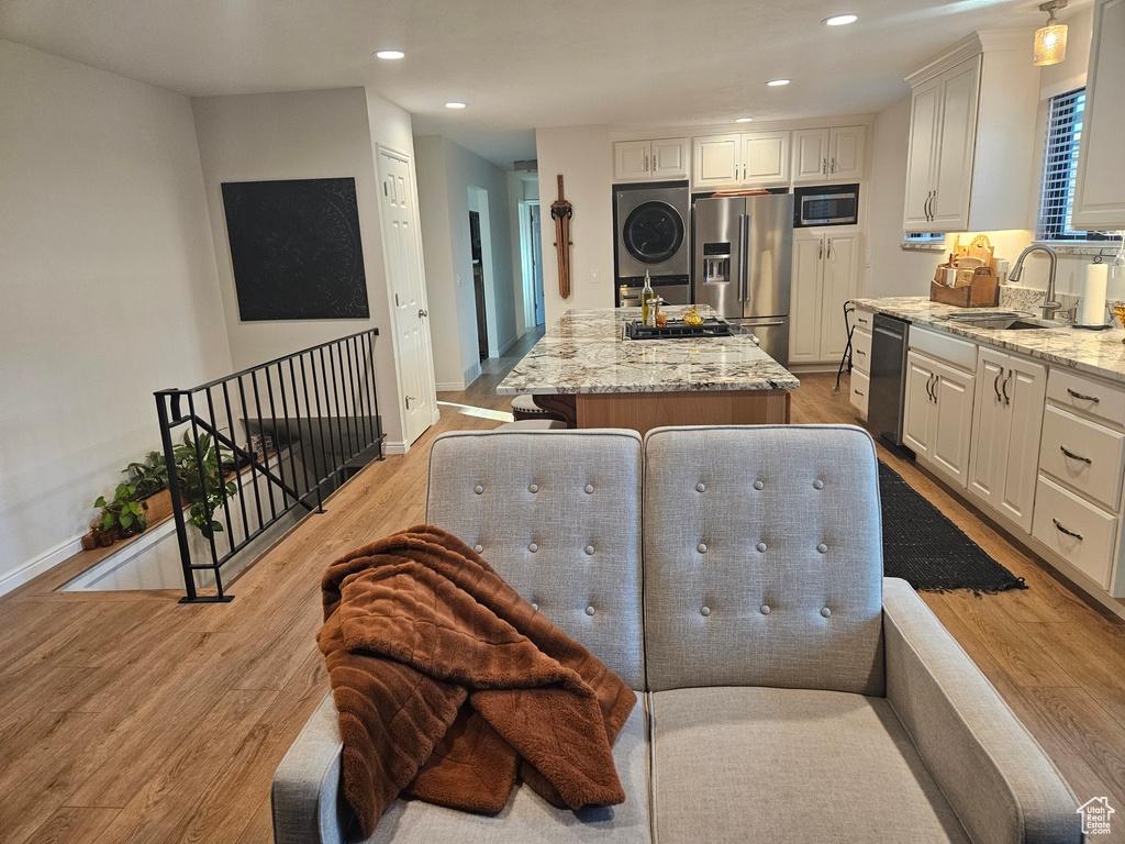 Kitchen with appliances with stainless steel finishes, stacked washer and clothes dryer, a sink, a center island, and light stone counters