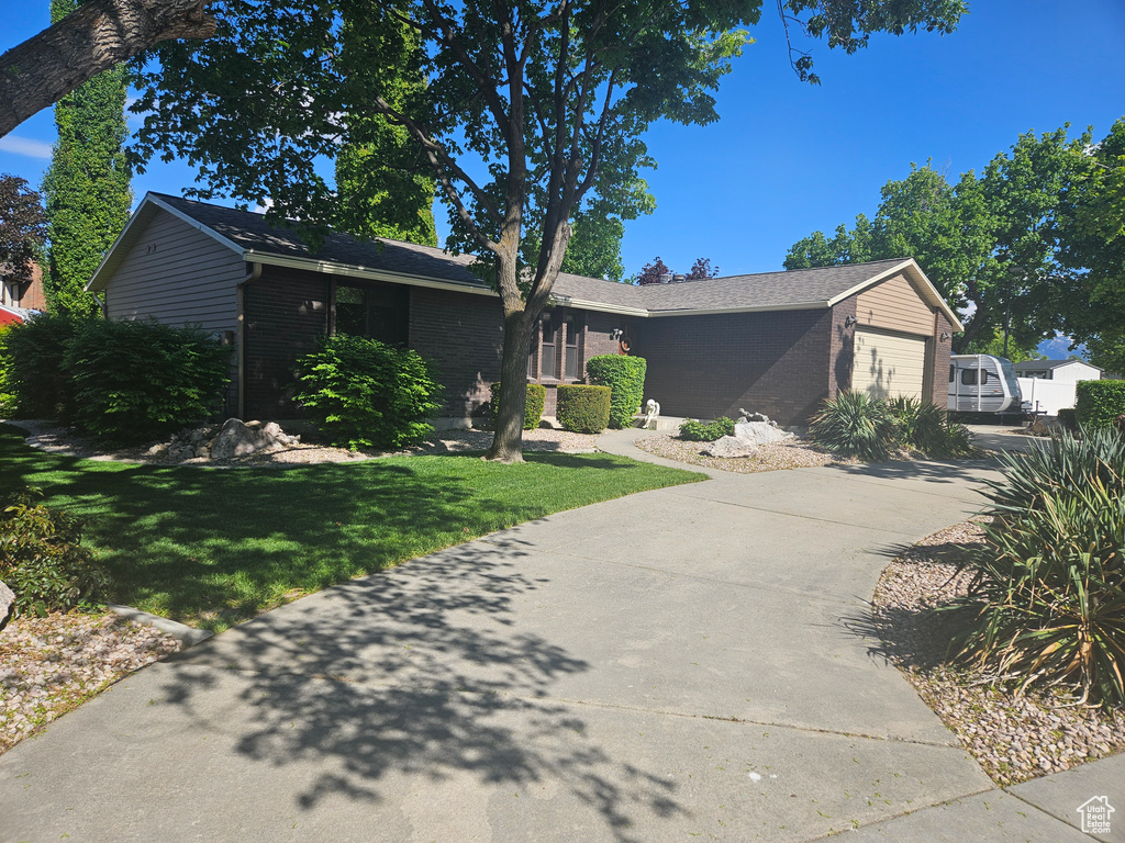 View of front of home with driveway, a garage, brick siding, and a front yard