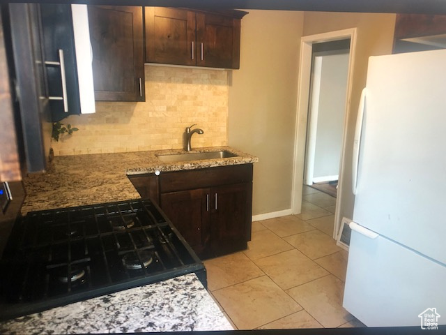 Kitchen with freestanding refrigerator, a sink, backsplash, dark brown cabinetry, and black range with gas stovetop