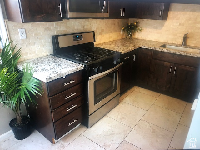Kitchen with stainless steel appliances, a sink, decorative backsplash, and light stone countertops