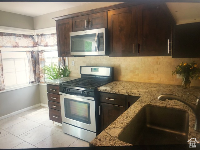 Kitchen featuring stainless steel appliances, a sink, decorative backsplash, and light stone counters
