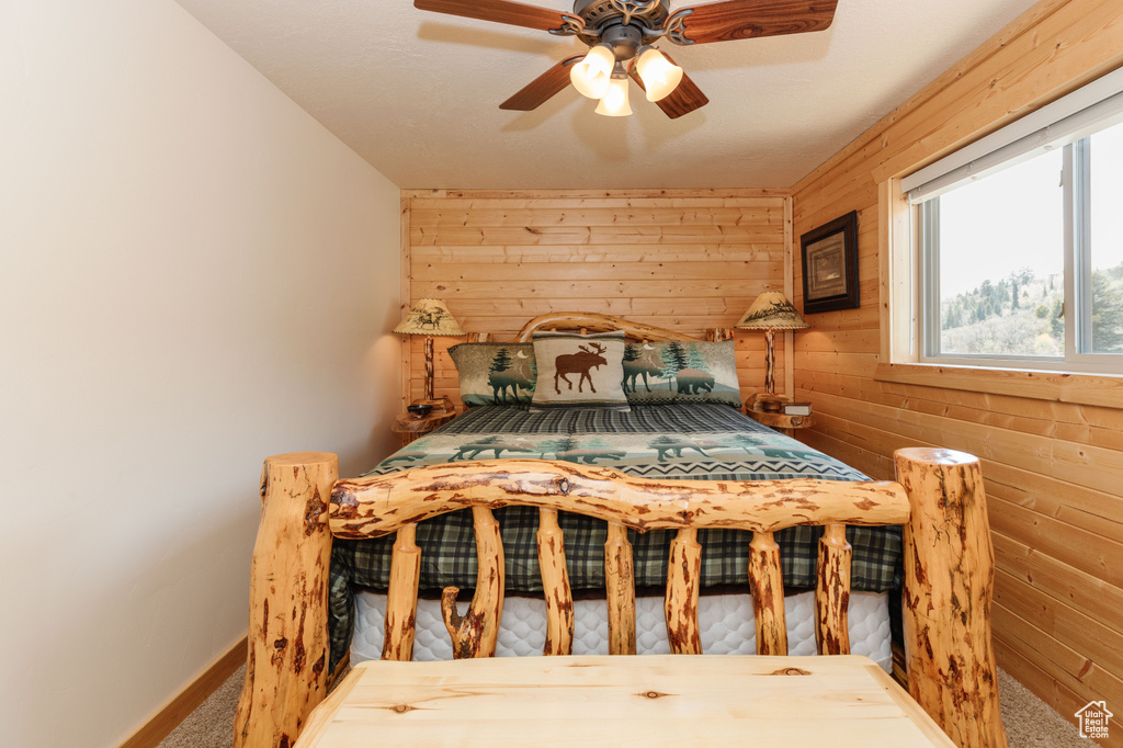 Carpeted bedroom with wooden walls, multiple windows, baseboards, and ceiling fan