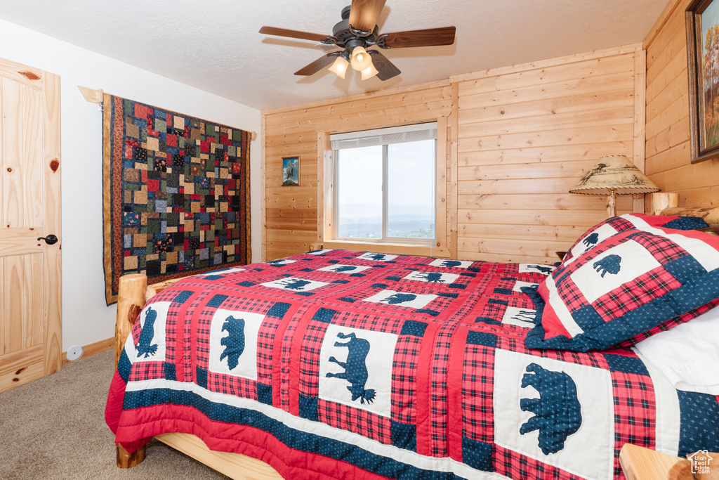 Carpeted bedroom featuring wooden walls and ceiling fan