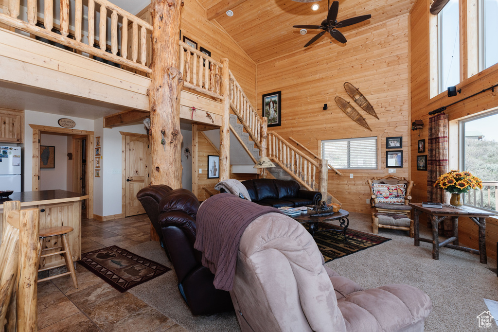 Living room featuring high vaulted ceiling, wooden walls, stairs, ceiling fan, and wooden ceiling
