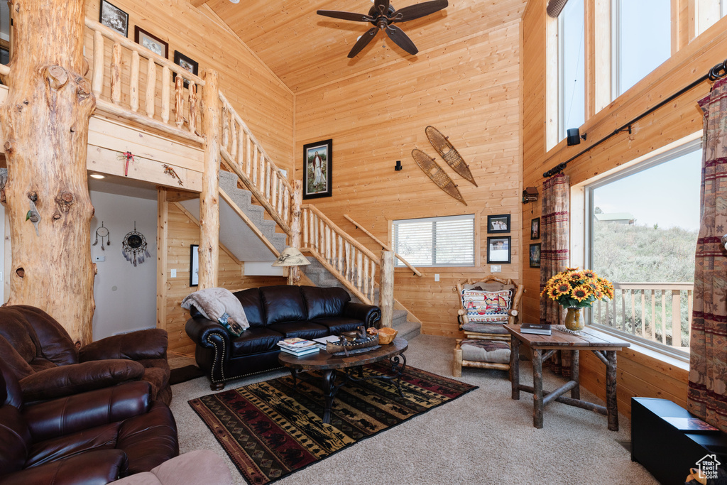 Carpeted living area featuring high vaulted ceiling, wood walls, wood ceiling, stairway, and ceiling fan