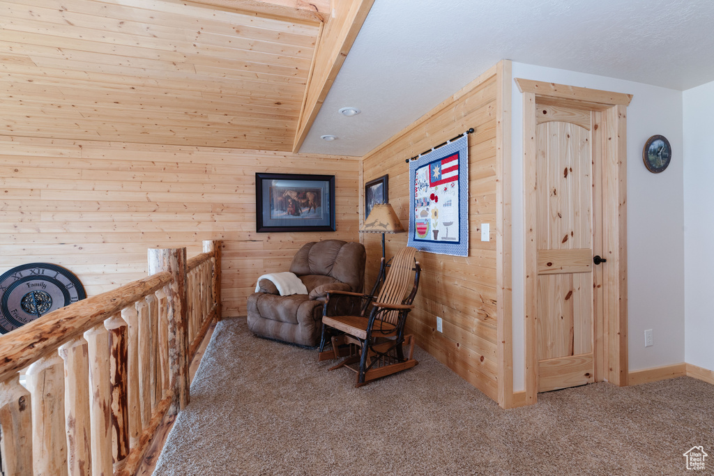 Sitting room featuring carpet floors, wooden walls, and an upstairs landing