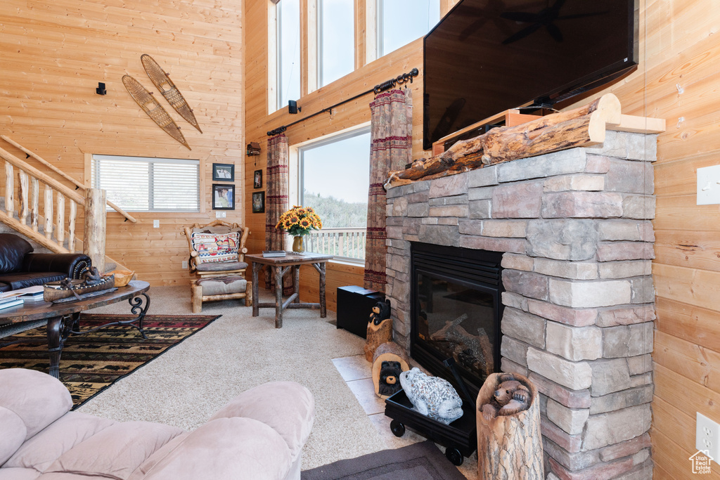 Living room with wood walls, carpet flooring, stairs, a stone fireplace, and a high ceiling