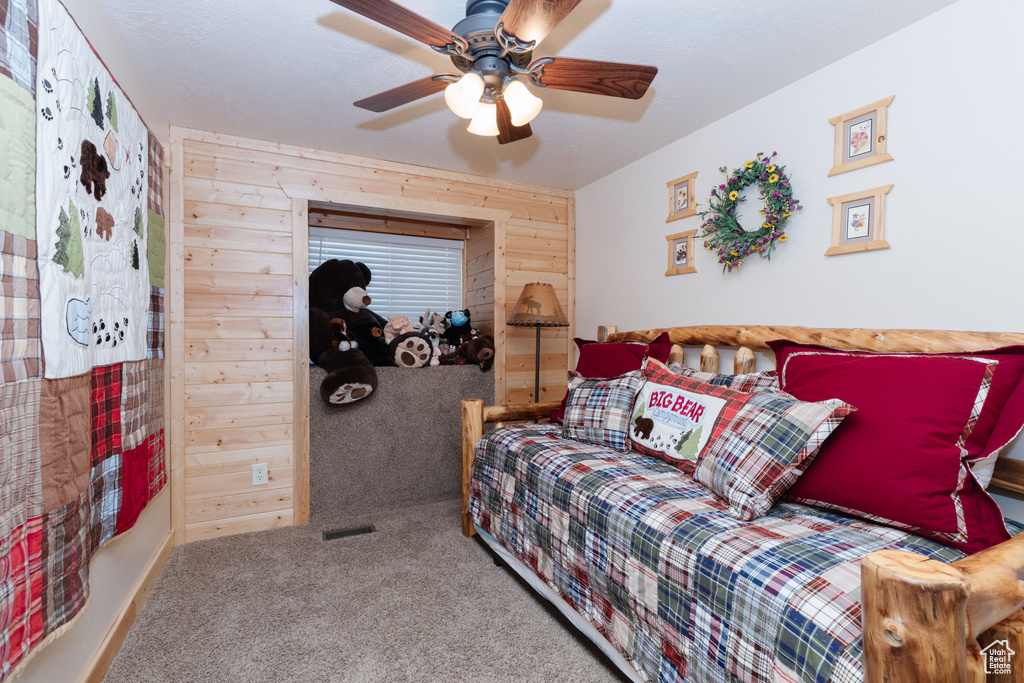 Carpeted bedroom with wood walls and a ceiling fan