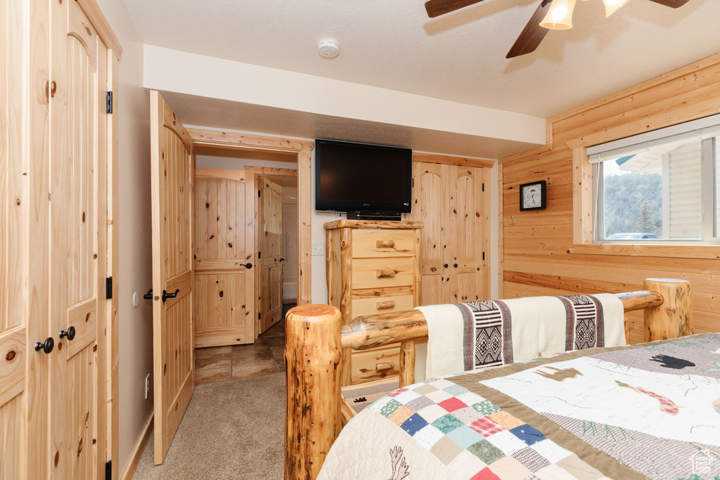 Bedroom featuring light colored carpet, a ceiling fan, wooden walls, and a closet
