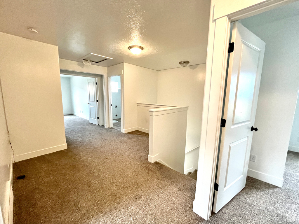 Hallway with an upstairs landing, carpet flooring, attic access, baseboards, and a textured ceiling