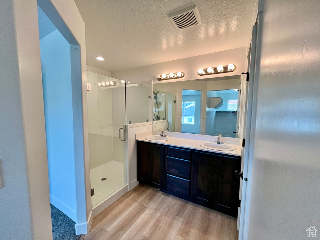 Bathroom with wood finished floors, double vanity, a shower stall, a textured ceiling, and baseboards