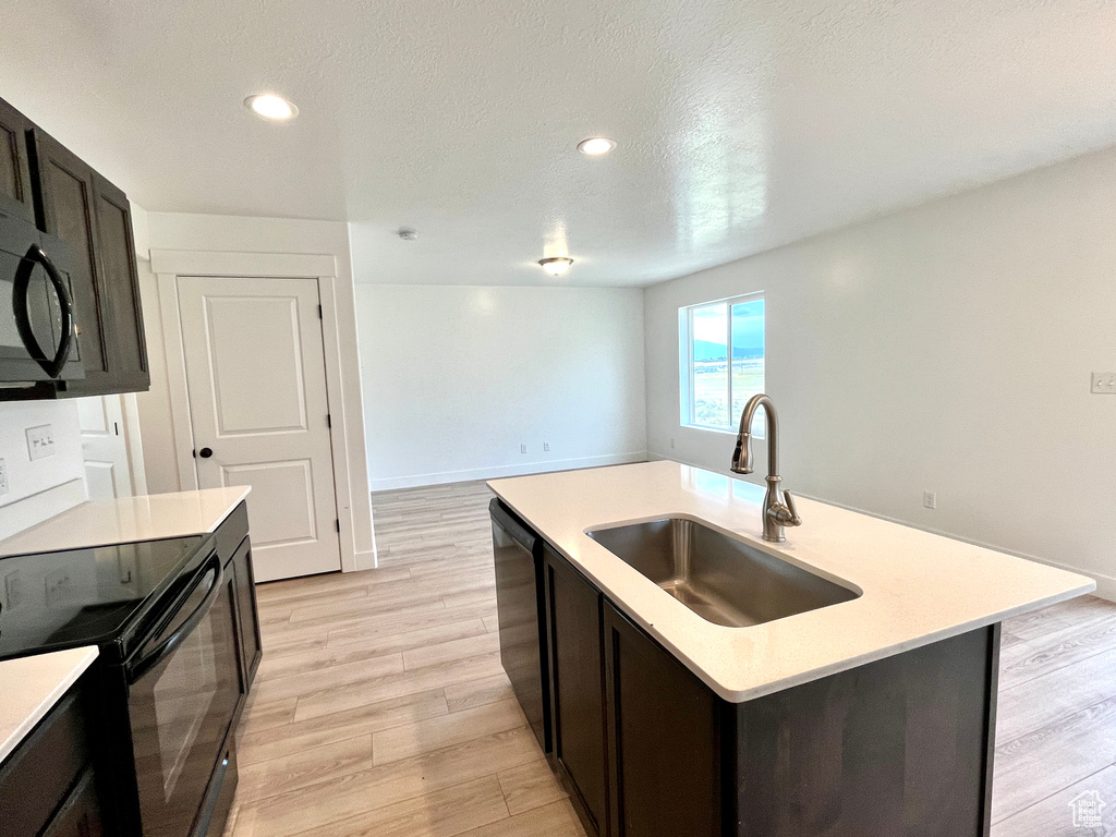 Kitchen with a sink, black appliances, light countertops, light wood finished floors, and recessed lighting