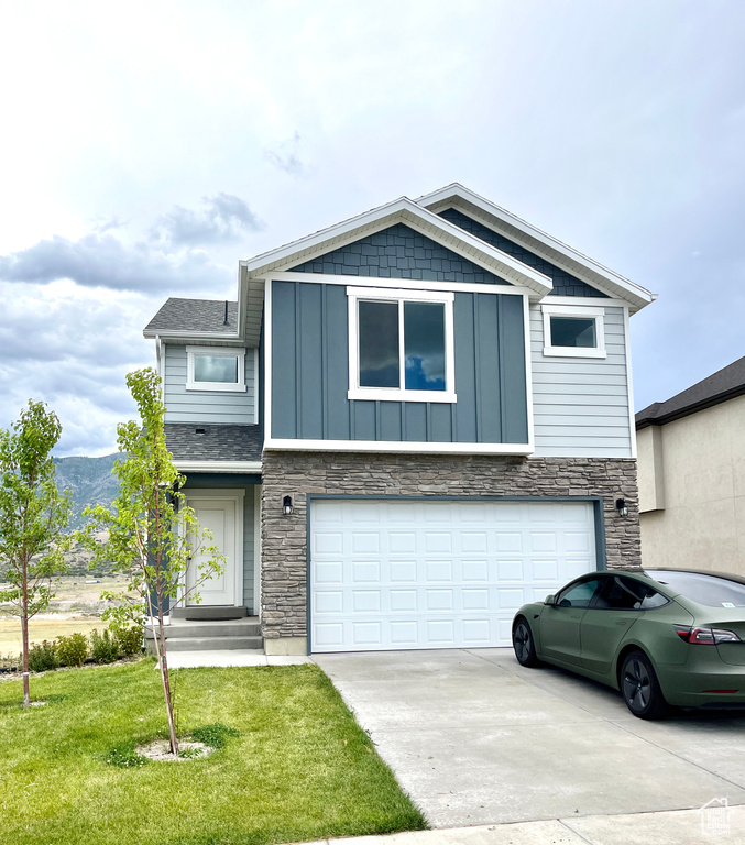 View of front facade with board and batten siding, an attached garage, driveway, and stone siding