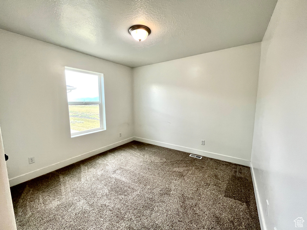 Unfurnished room with dark carpet, baseboards, and a textured ceiling