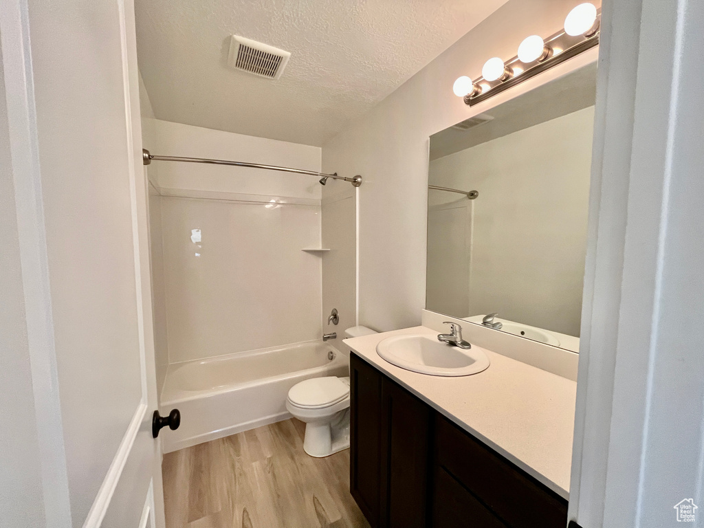 Bathroom with wood finished floors, washtub / shower combination, vanity, toilet, and a textured ceiling