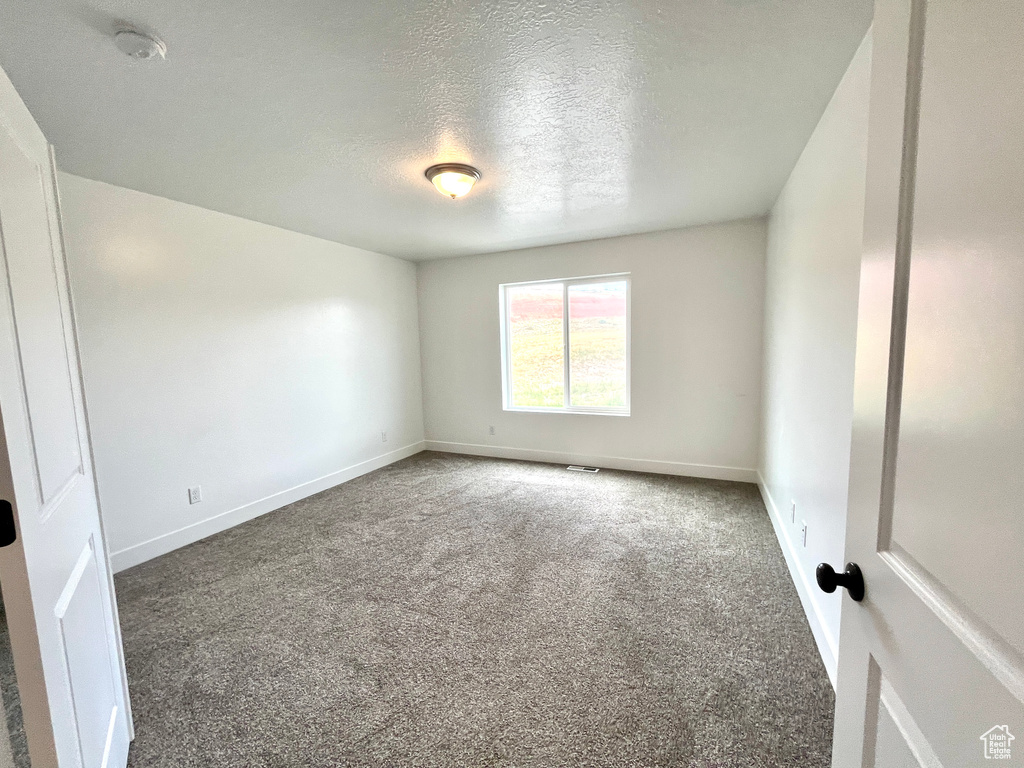 Carpeted empty room with baseboards, a textured ceiling, and a smoke detector