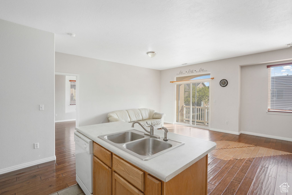 Kitchen featuring white dishwasher, open floor plan, a sink, wood finished floors, and light countertops