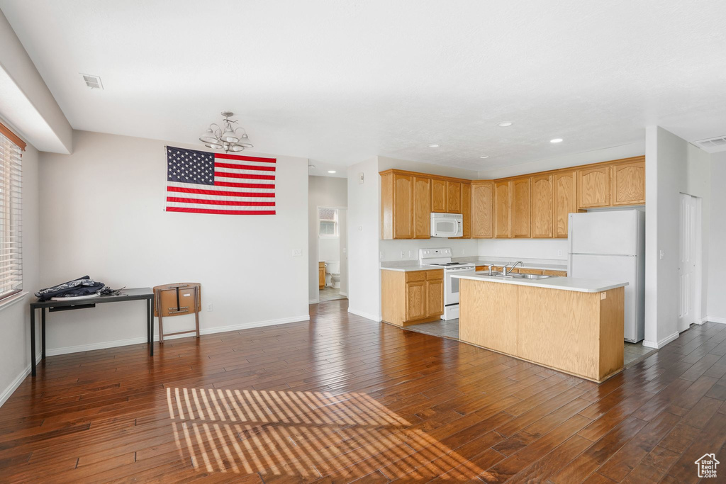Kitchen with white appliances, dark wood finished floors, light countertops, a center island with sink, and a chandelier
