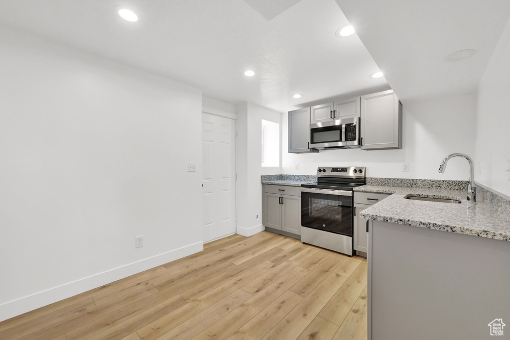 Kitchen with appliances with stainless steel finishes, a sink, gray cabinets, light wood finished floors, and recessed lighting