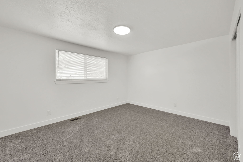 Unfurnished room with dark carpet, baseboards, and a textured ceiling