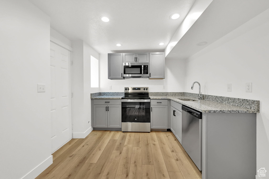 Kitchen with appliances with stainless steel finishes, a sink, gray cabinetry, light wood finished floors, and recessed lighting